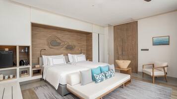 Un dormitorio moderno con una cama grande, cabecera de madera, ventilador de techo, televisor y un espacio de descanso con una silla y una mesita.