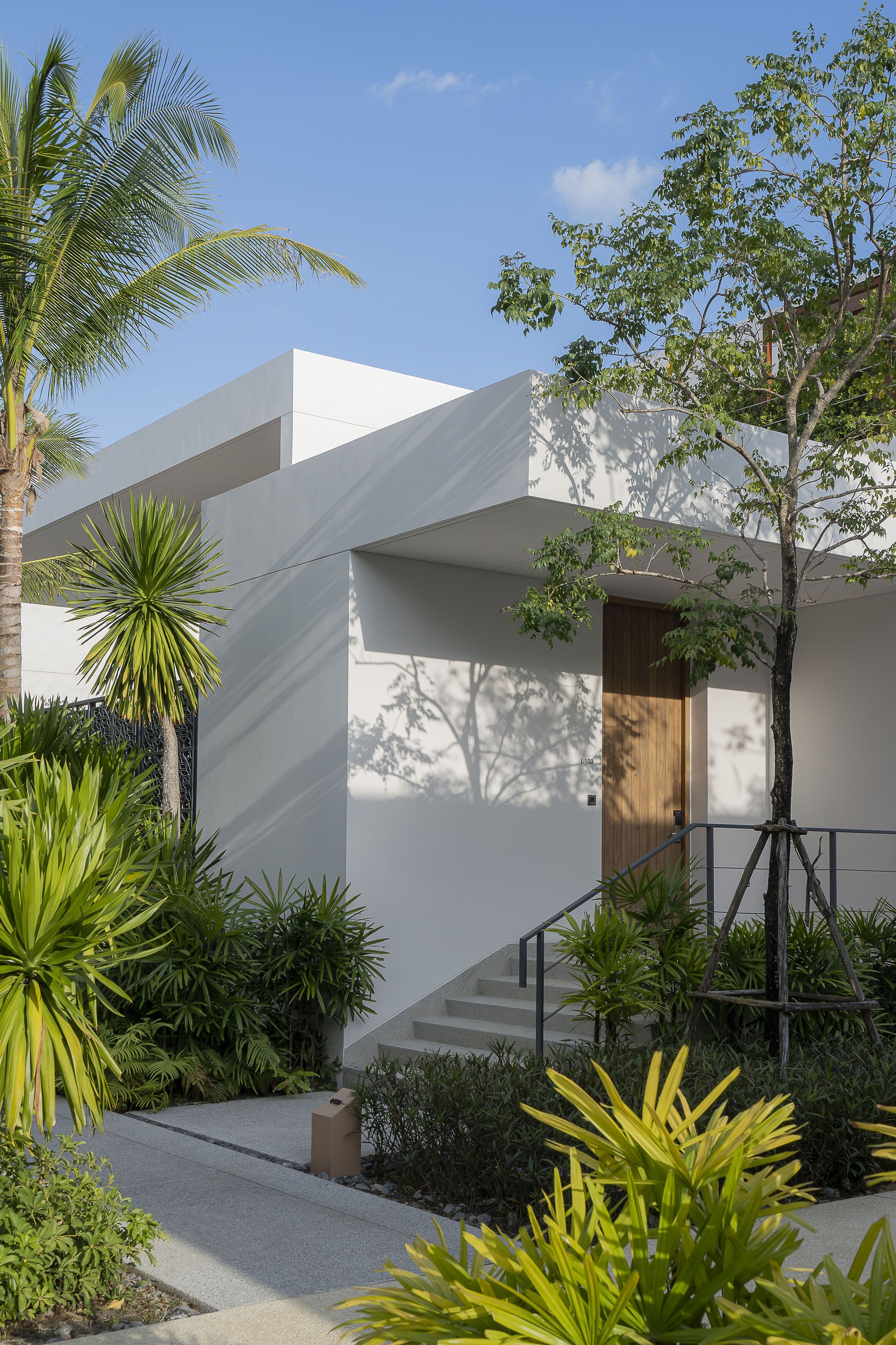 A modern building with a staircase, surrounded by lush greenery and palm trees.