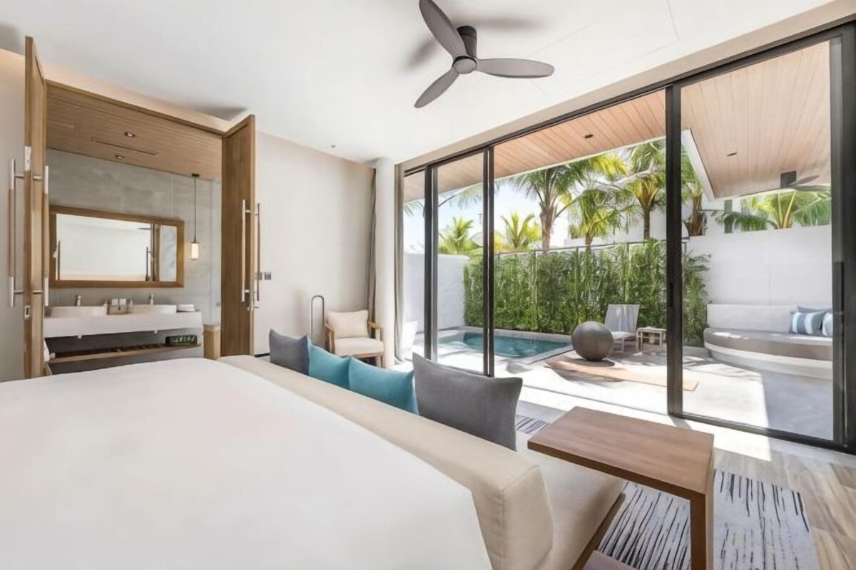 Een moderne hotelkamer met een groot bed, een badkamer met spiegel en uitzicht op een zwembad.