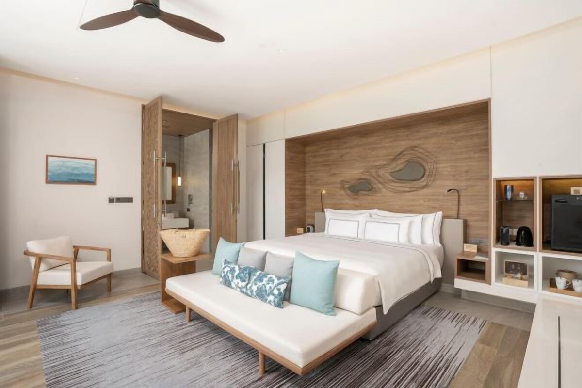 Ett modernt hotellrum med en säng, en sittgrupp, en sminkbord och en inbyggd hyllsektion.