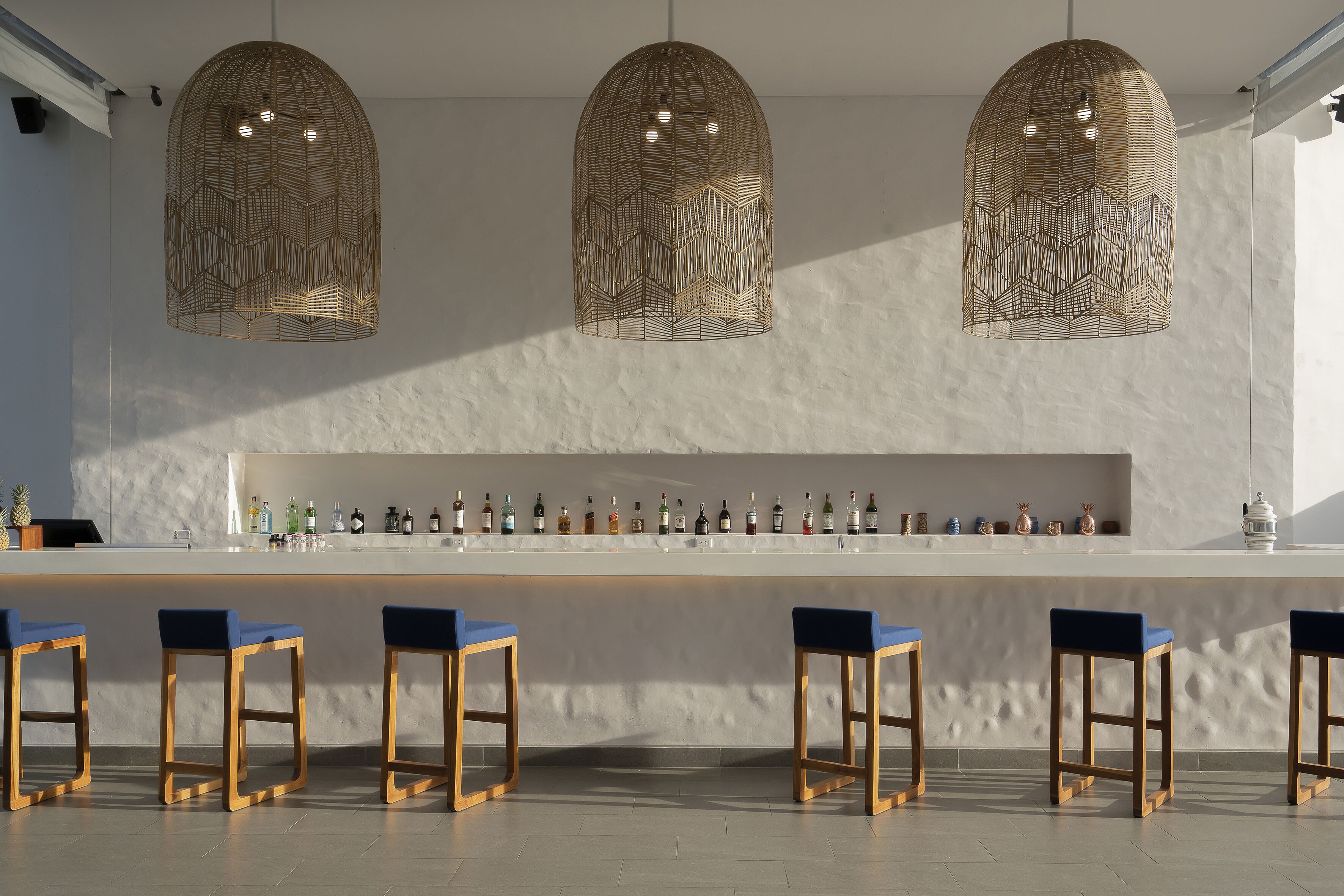 A bar area with three hanging pendant lights, a white marble countertop, and six blue bar stools.