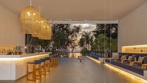 A modern bar area with a long counter, wooden stools, and a seating area with cushions and a wooden table. - Melia Phuket Mai Khao (Mai Khao)