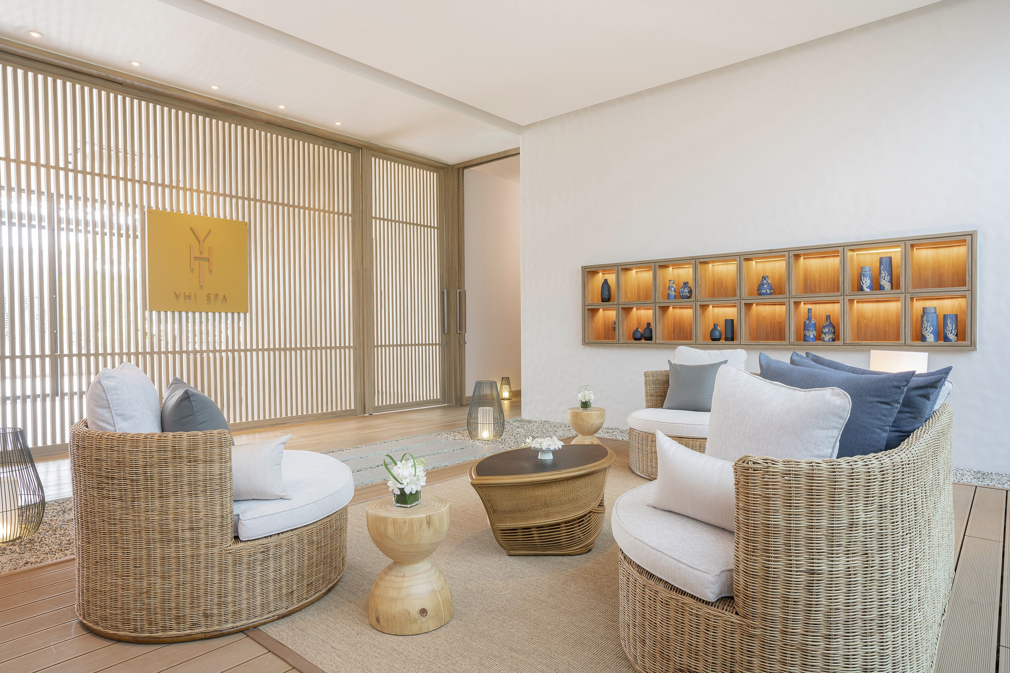 A modern lounge area with wicker furniture, a wall-mounted display of vases, and a sliding door with vertical blinds.
