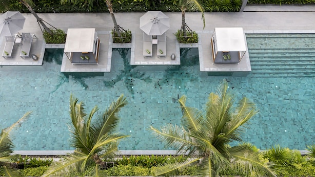 An aerial view of a pool area with lounge chairs and umbrellas, surrounded by lush greenery. - Melia Phuket Mai Khao (Mai Khao)