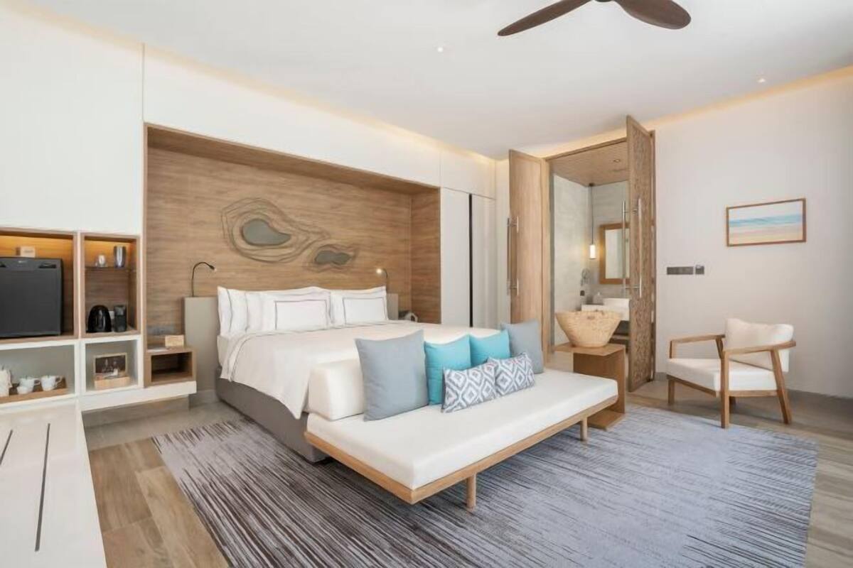 Quarto moderno com cama, mesas de cabeceira, televisão e área de estar.