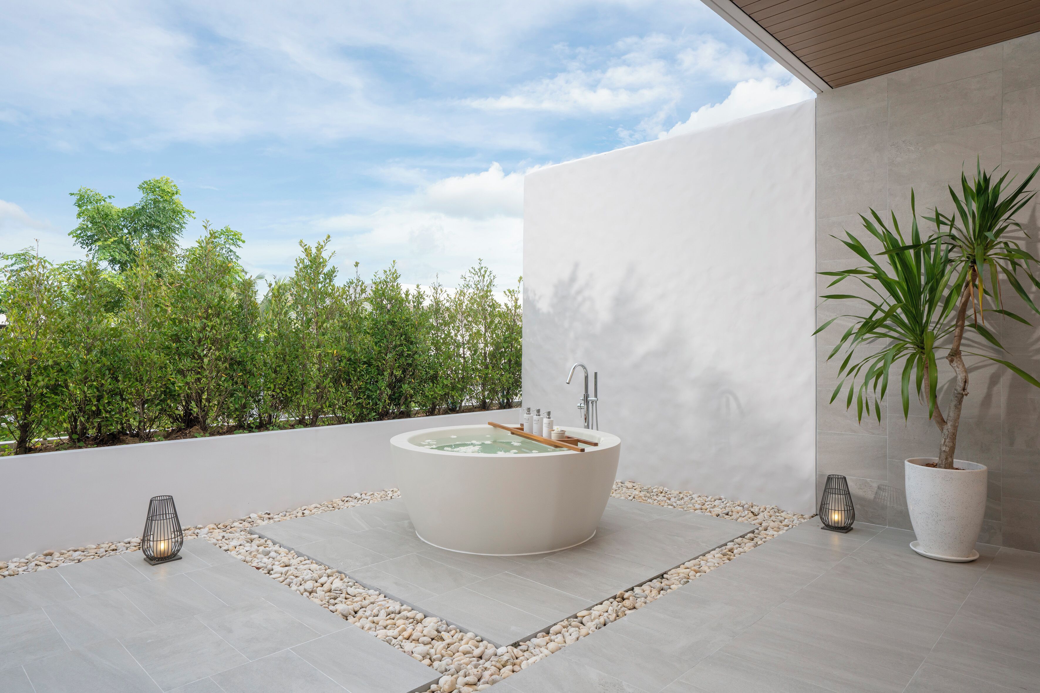 A modern outdoor bathtub with a view of trees and a clear sky.