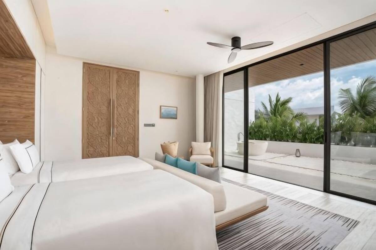 Quarto de hotel moderno com uma cama grande, um sofá, uma varanda com vista e um ventilador de teto.