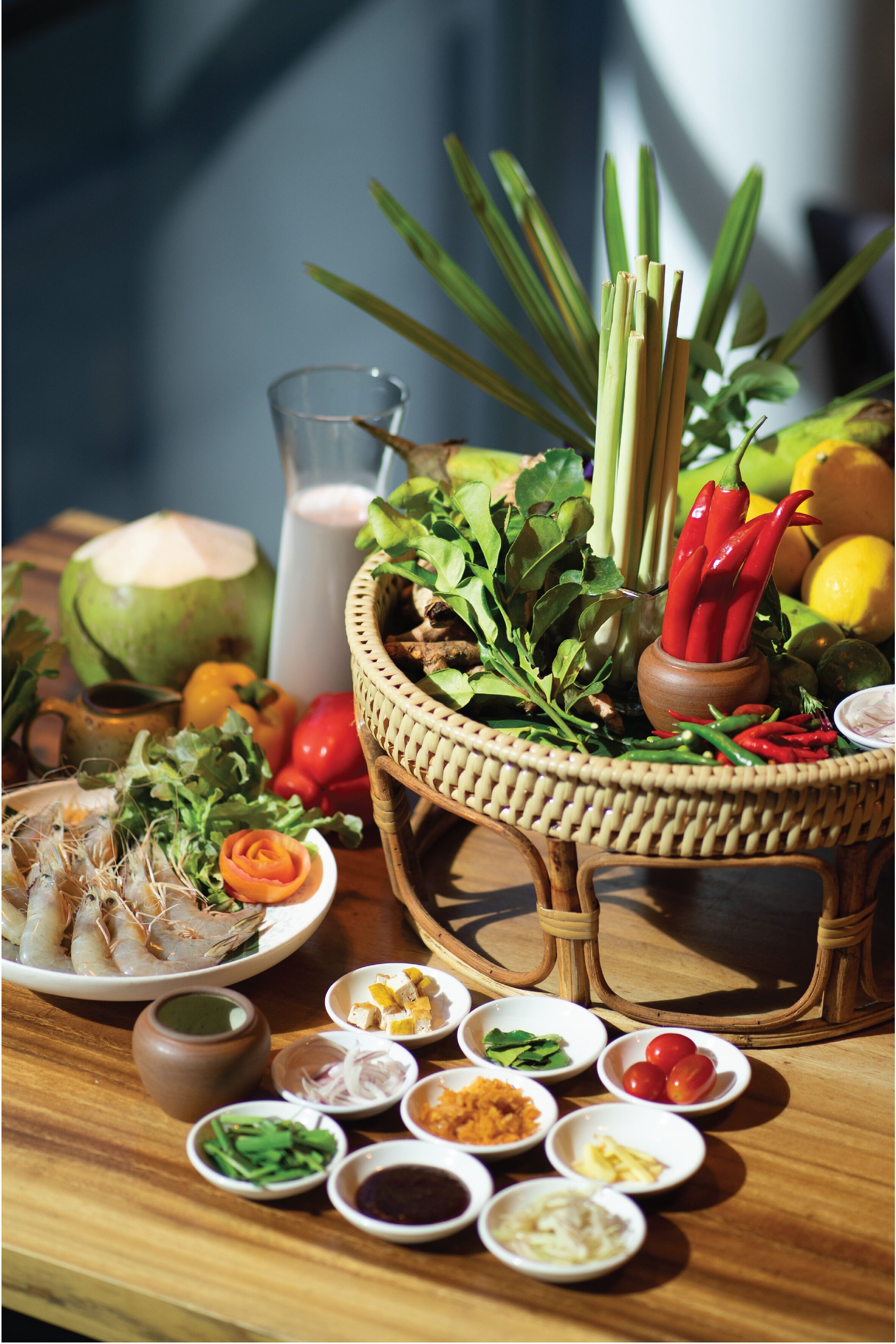 Une table garnie de divers aliments et condiments, notamment un panier d’herbes fraîches, des légumes et une assiette de fruits de mer.