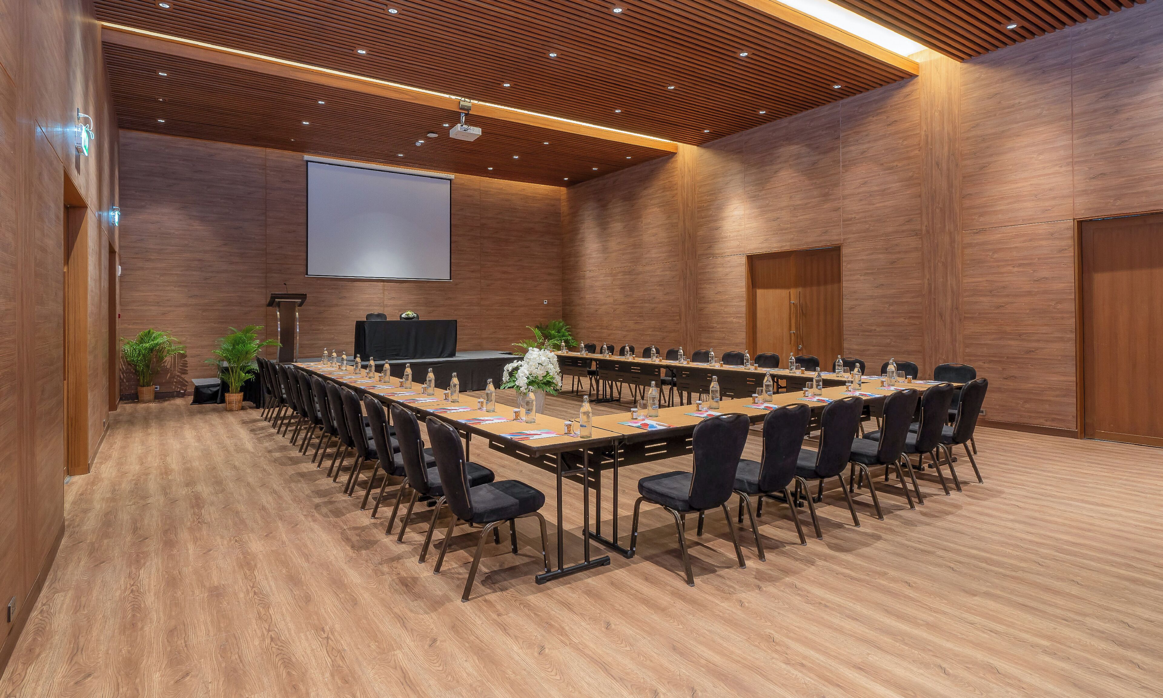 Una sala de conferencias con una larga mesa, sillas, una pantalla de proyector y un atril.