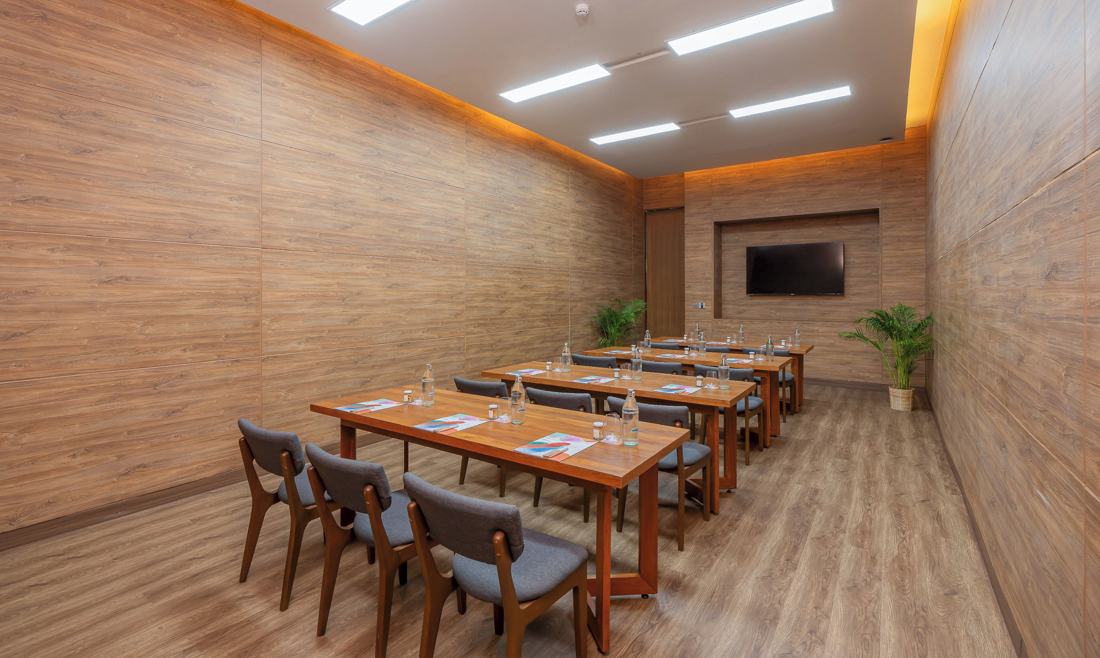 A conference room with wooden walls, a flat-screen TV mounted on the wall, and multiple tables with chairs.