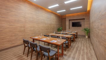 A conference room with wooden walls, a flat-screen TV mounted on the wall, and multiple tables with chairs.