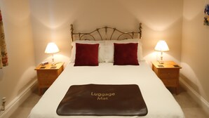 A neatly made bed with a luggage mat labeled "Luggage Mat" in a hotel room with two bedside tables, each with a lamp and a phone. - Oak End Lodge (Sevenoaks)