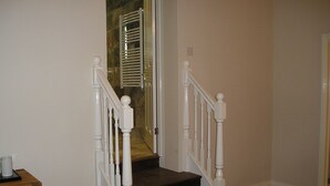 A staircase with white balusters and dark steps leading to a room with a wooden dresser and a white lamp. - Oak End Lodge (Sevenoaks)