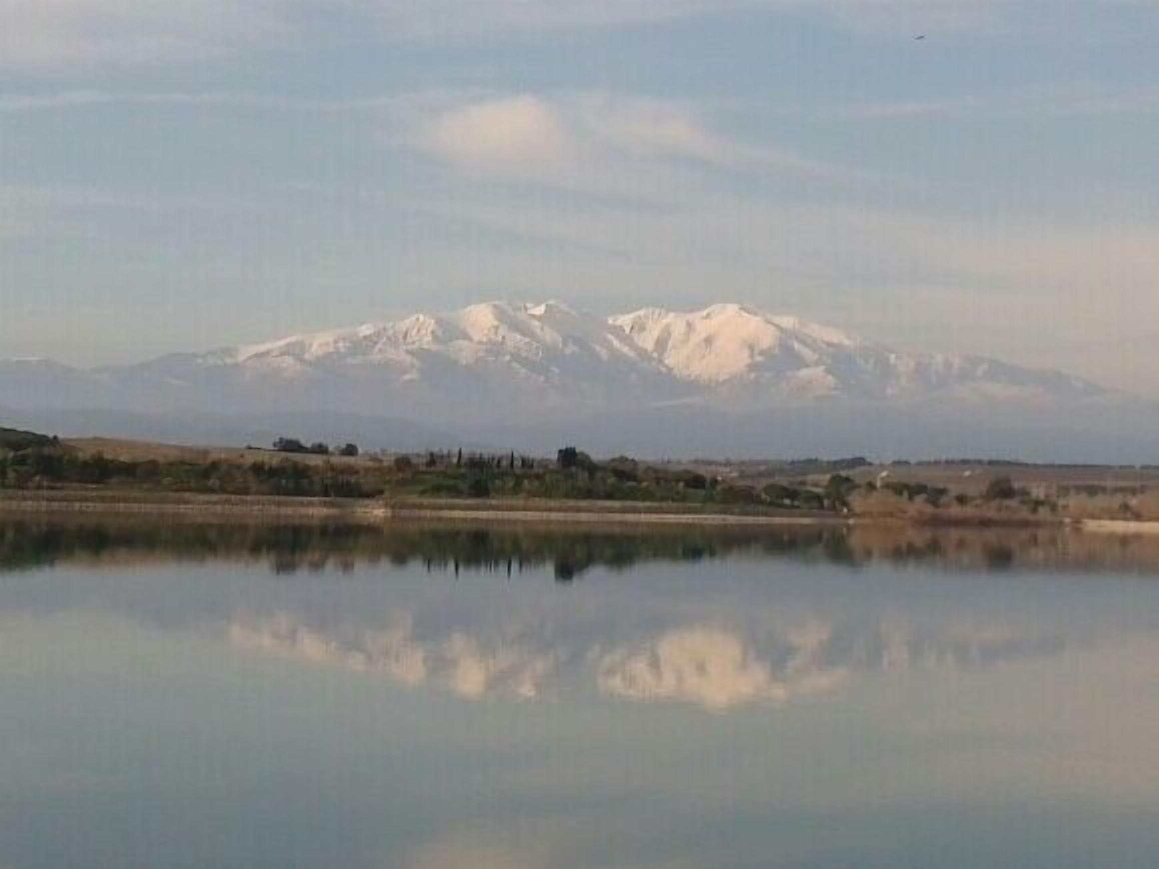 A mountain range reflected in a calm body of water, with a flat landscape in the foreground.