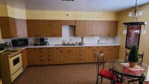 Una cocina compacta con armarios de madera, microondas, estufa y comedor con mesa de vidrio y sillas de metal.