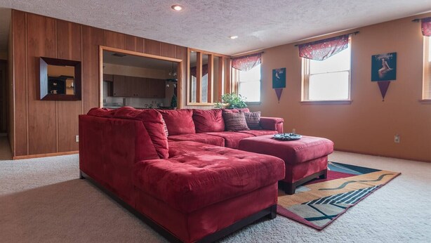 Una sala de estar con un sofá seccional rojo, un espejo grande y vista a la cocina por una puerta abierta.