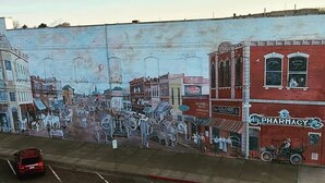 Un mural que representa una escena callejera histórica con varios edificios y gente.