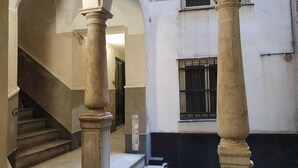 Un pasillo con columnas, una escalera y una ventana con barrotes.