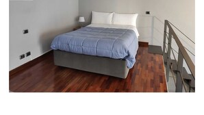 Un dormitorio con una cama, una mesita de noche, una lámpara y suelo de madera.