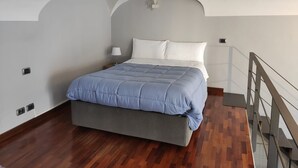A bedroom with a bed, a nightstand, a lamp, and a wooden floor.