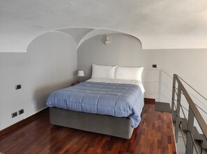 A bedroom with a bed, a nightstand, a lamp, and a wooden floor.