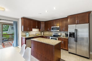 A modern kitchen with wooden cabinets, stainless steel appliances, and a granite countertop.