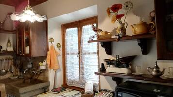 Una cucina rustica con mobili in legno, un vecchio piano cottura e una finestra con tende in pizzo.