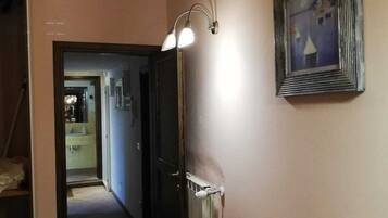 Un corridoio con una porta che dà su un bagno, un tavolino con una ciotola e una lampada a parete.