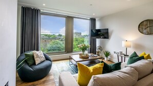 A modern living room with a large window, a flat-screen TV, and a cozy seating area.