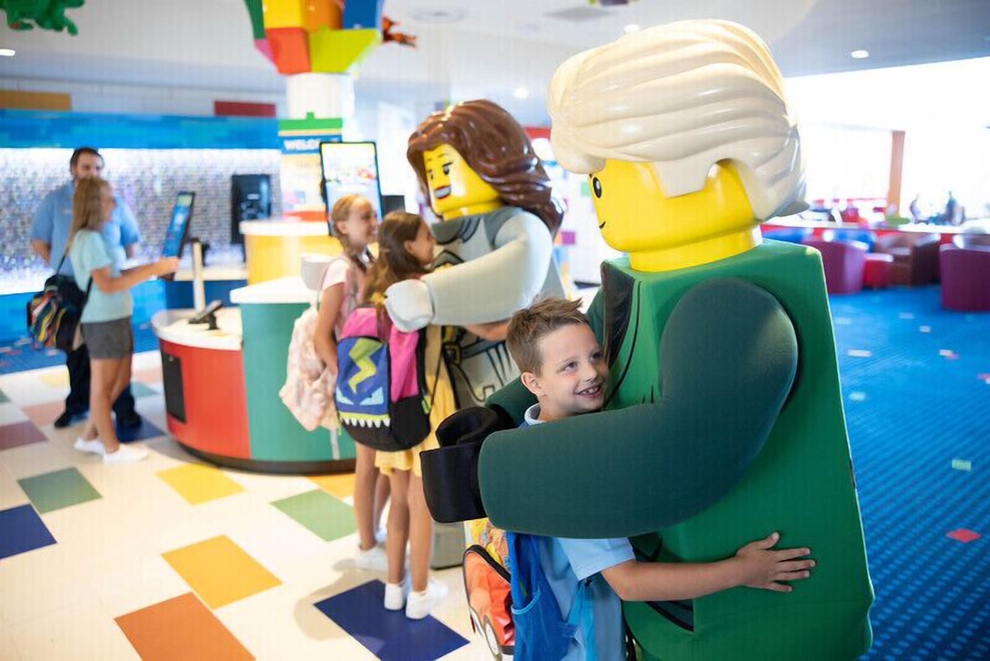 A child being embraced by a LEGO figure in a colorful indoor play area.