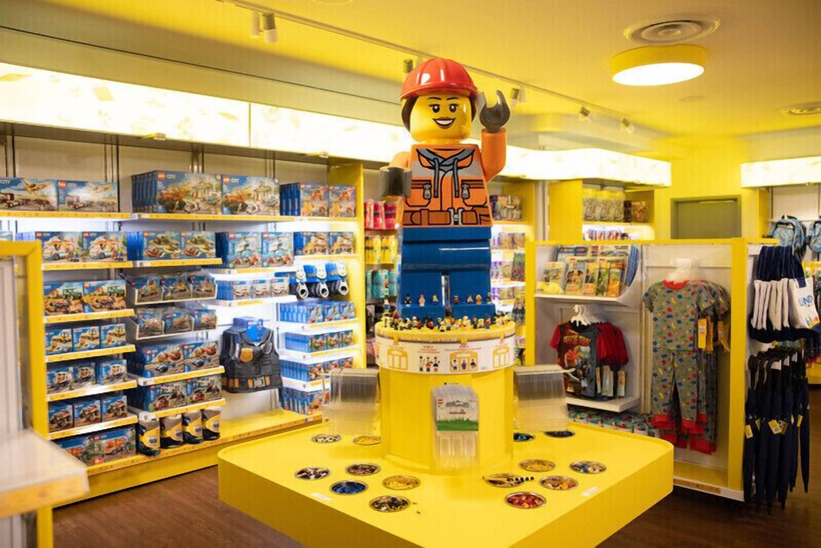 Un magasin de jouets avec des étagères remplies de jouets et une grande figurine LEGO exposée.