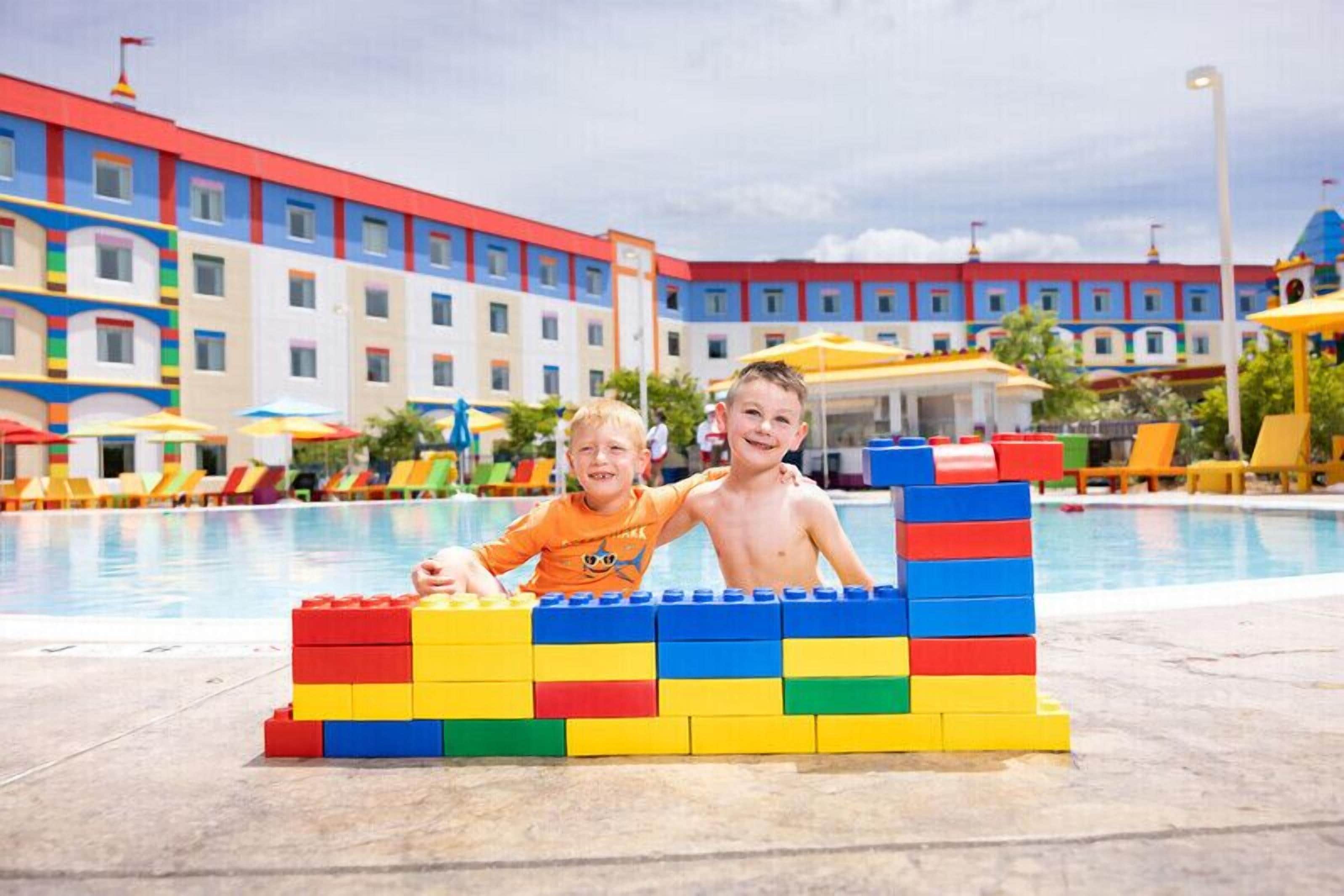 A pool area with colorful building facades and a children's play structure made of interlocking blocks.