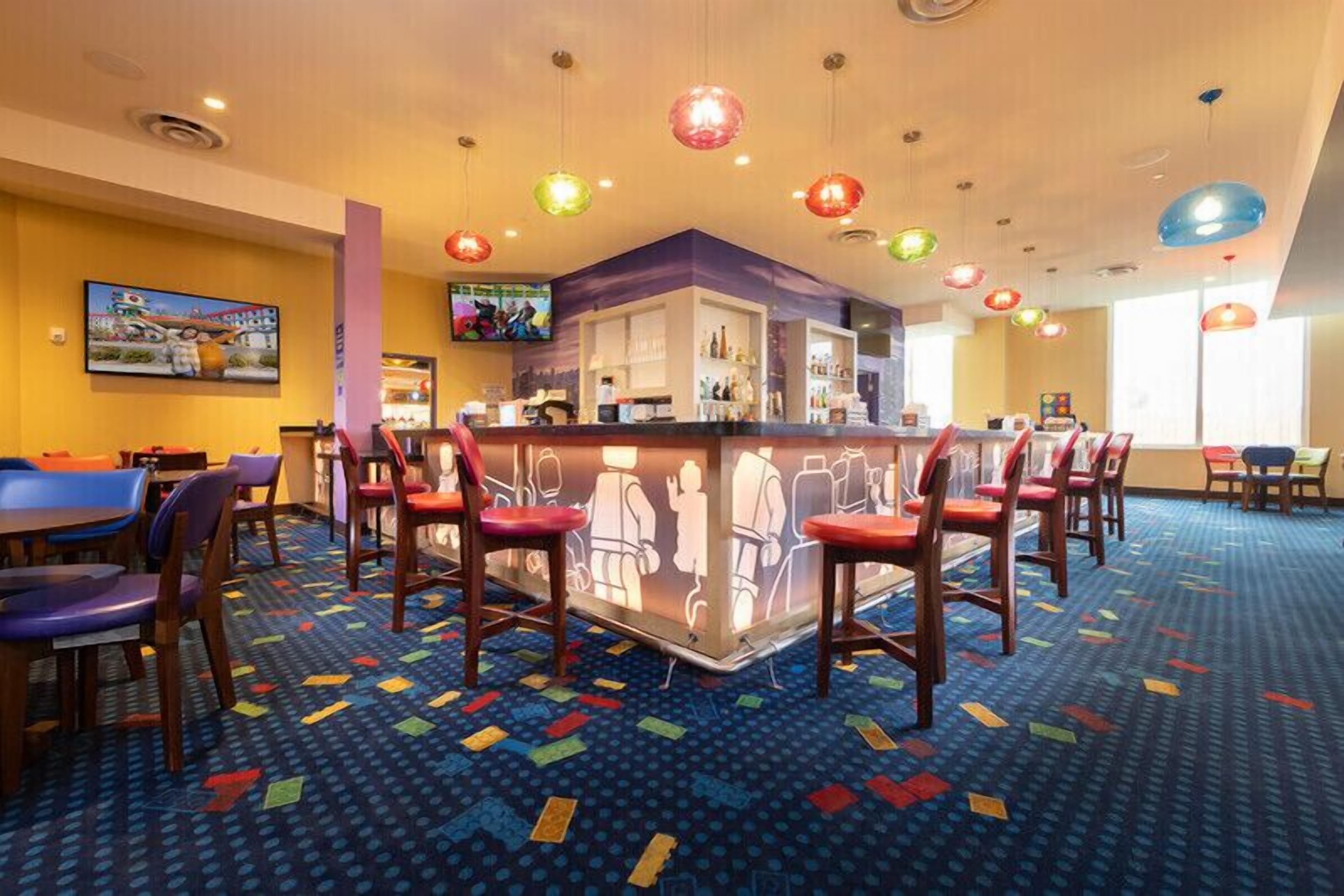 A hotel lobby with a bar area, colorful patterned carpet, and multiple seating options including chairs and tables.