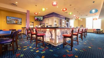 A hotel lobby with a bar area, colorful patterned carpet, and multiple seating options including chairs and tables.