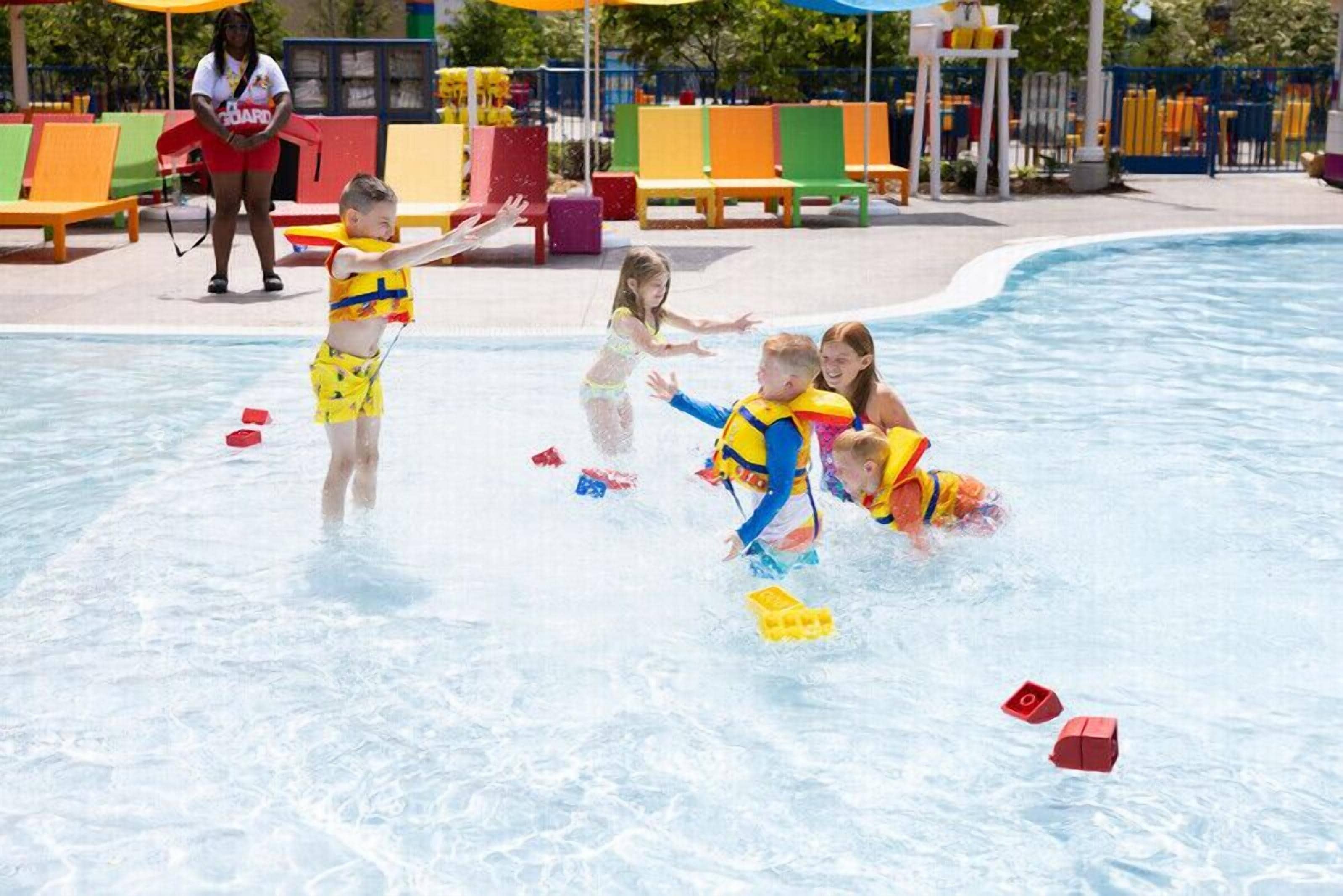 A swimming pool area with children playing and a lifeguard present.