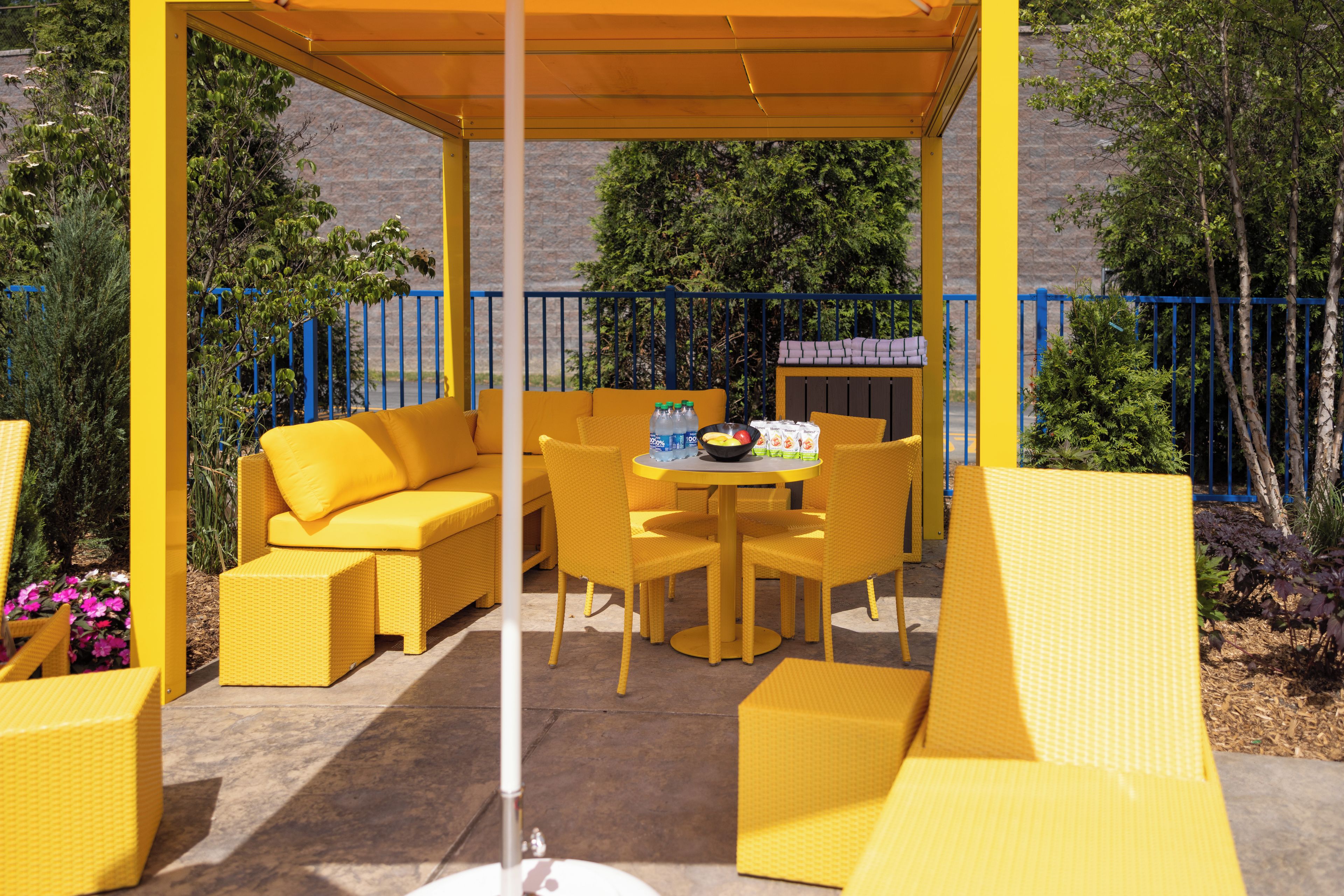 A covered patio area with yellow wicker furniture, including a sofa, chairs, and a table.