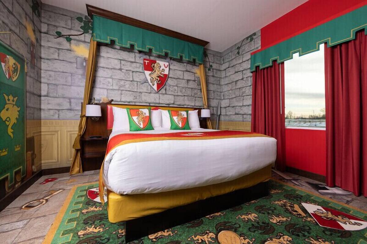A hotel room with a large bed, a stone wall, a window with red curtains, and a shield emblem on the wall.