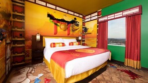 Una habitación de hotel con una cama grande, una estantería, un mural y una ventana con cortinas.