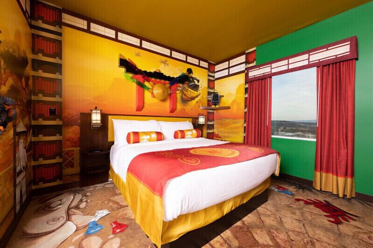 A hotel room with a large bed, a bookshelf, a mural, and a window with curtains.