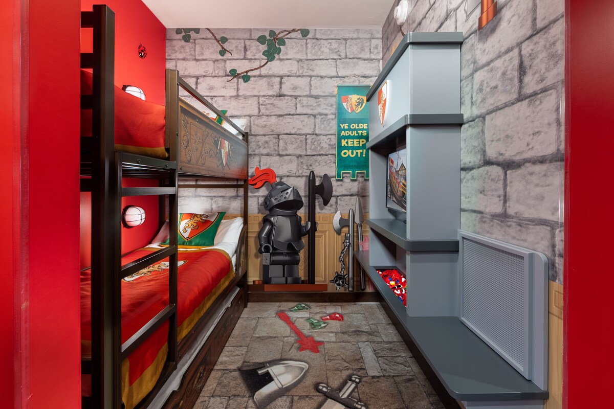A narrow room with bunk beds, a small table, and a wall-mounted shelf.