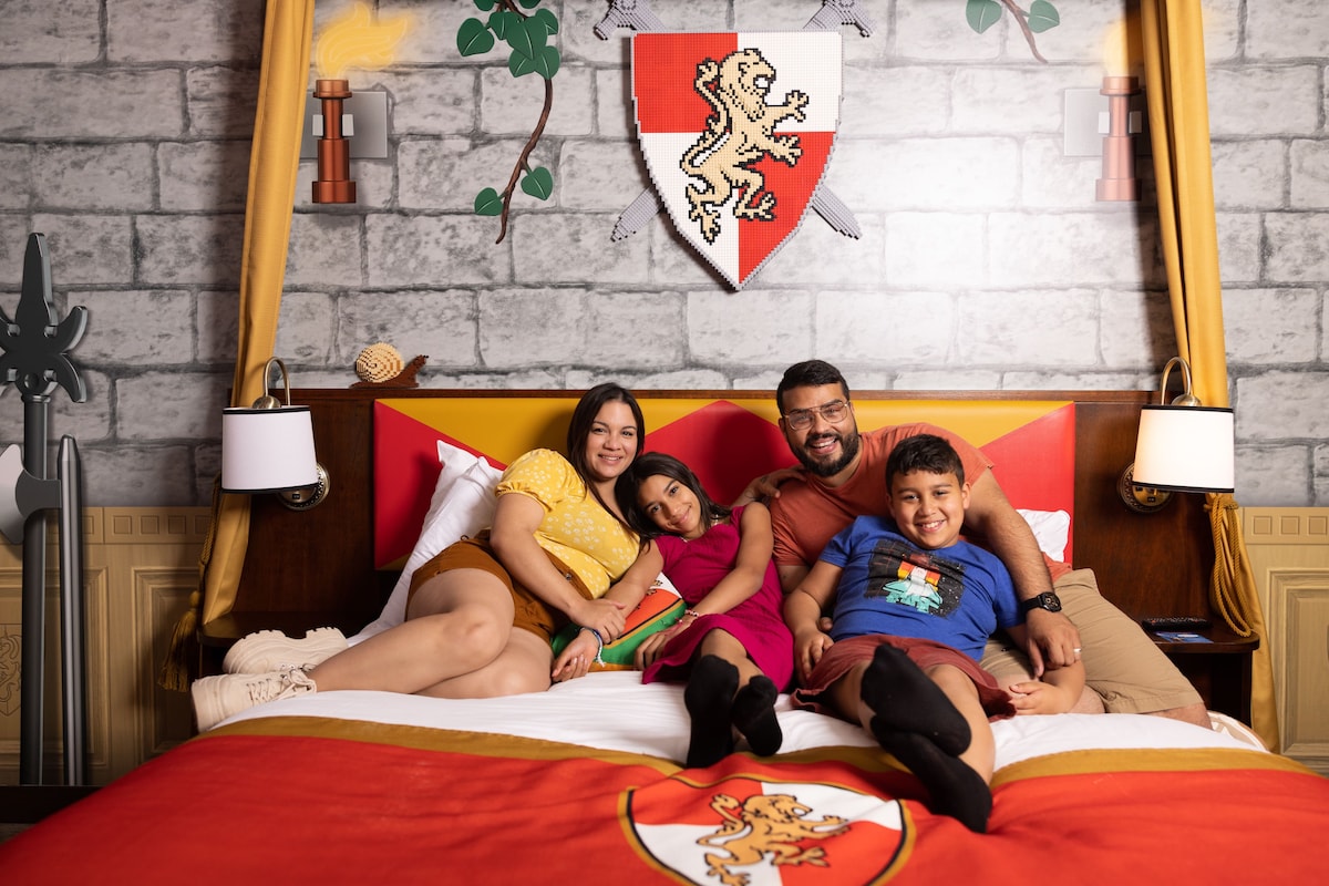 A bed with a red and white bedspread, a wooden headboard, and a wall-mounted shield with a lion emblem.