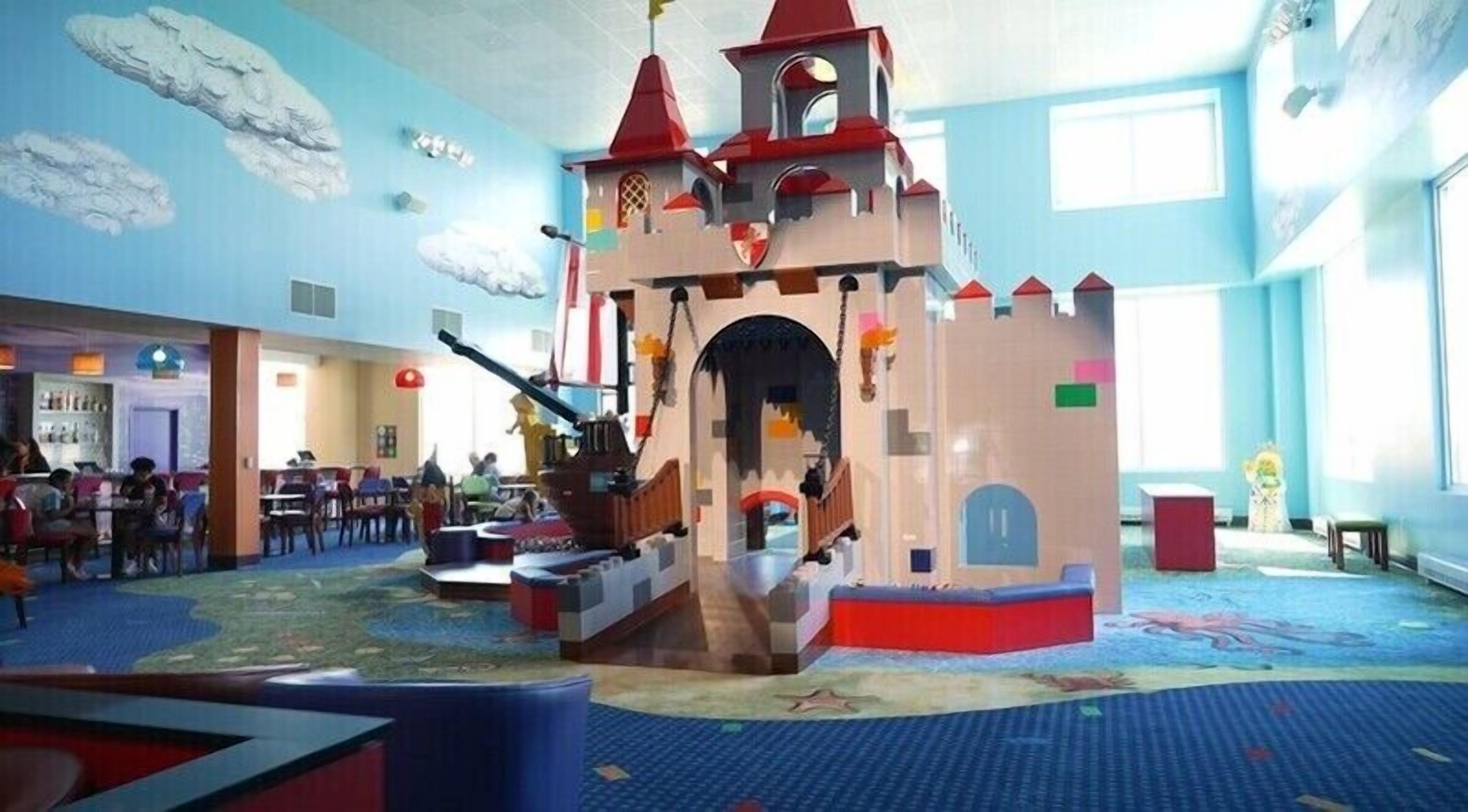 Un espace de jeux comprenant une structure en forme de château, un toboggan et une cuisine miniature.