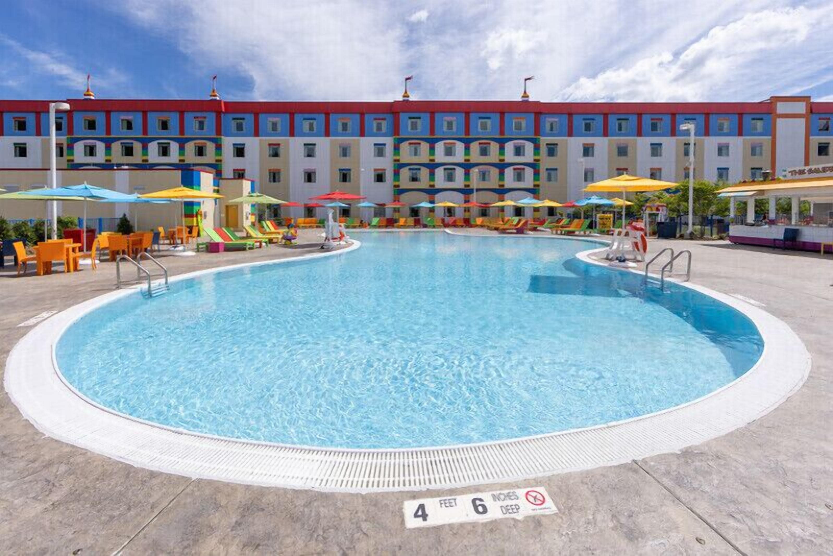 Una piscina con un cartel que indica una profundidad de 1 metro 37 centímetros, rodeada de sombrillas de colores y sillas reclinables.