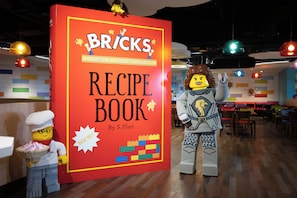 A LEGO display with a large red sign reading 'BRICKS RECIPE BOOK' by S. Platt, featuring LEGO figures and a colorful LEGO building. - LEGOLAND Hotel NEW York (Goshen)