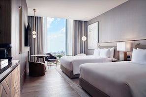 Quarto de hotel com duas camas, área de refeições, televisão e vista para a cidade.