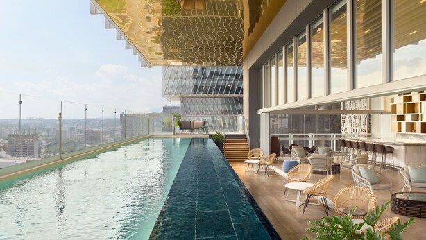 Una piscina infinita en la azotea con vistas a la ciudad, mobiliario cómodo y un diseño arquitectónico moderno.