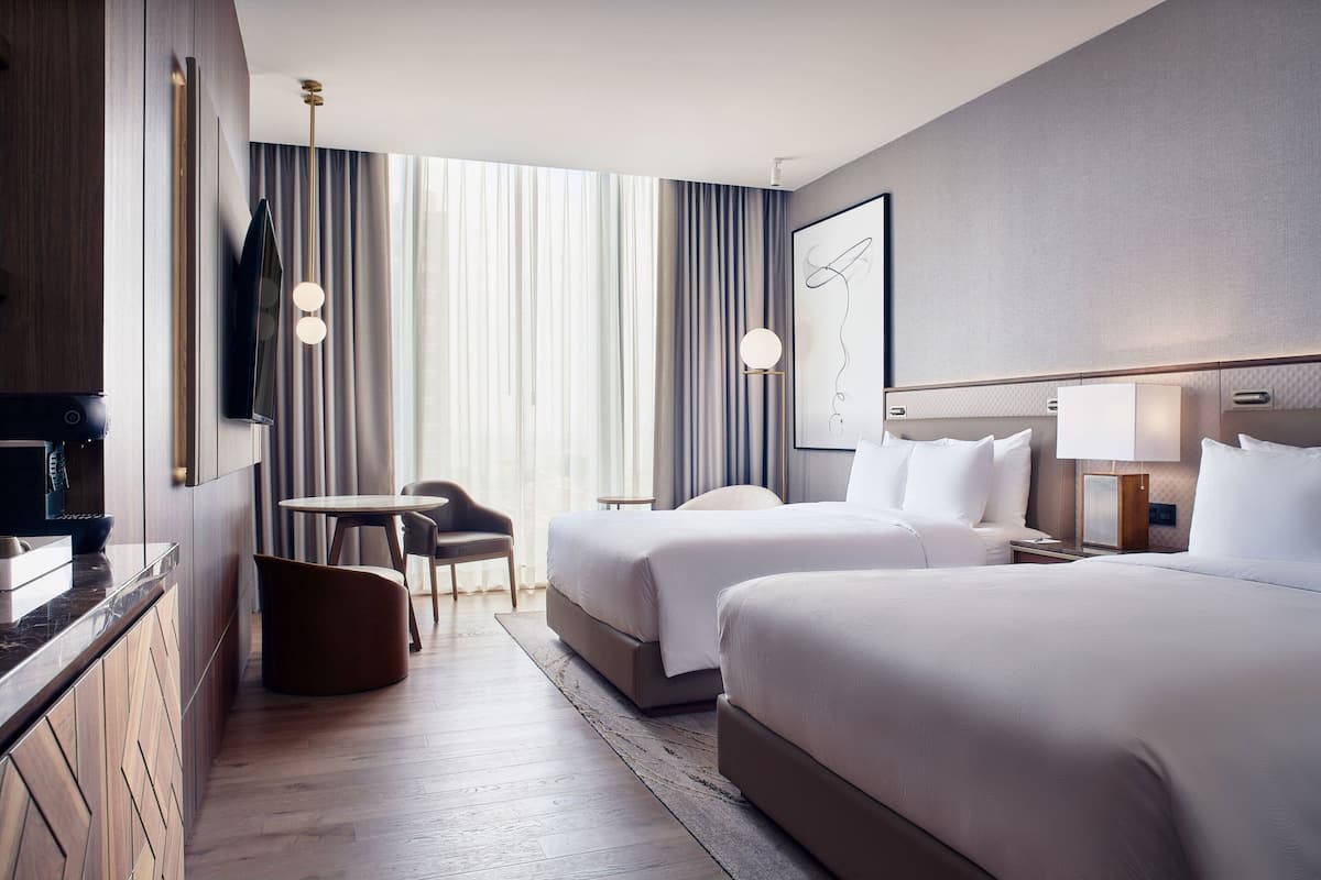Een hotelkamer met twee bedden, een bureau, een stoel, een televisie en een groot raam met gordijnen.