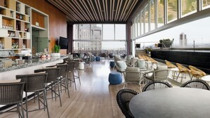 Un bar moderno con techos altos, paneles de madera y grandes ventanales con vistas a la ciudad.