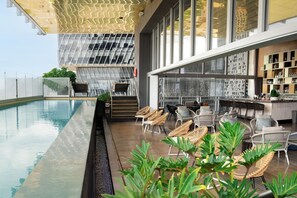 Um bar no terraço com piscina, cadeiras de vime e um espaço de bar com prateleiras.