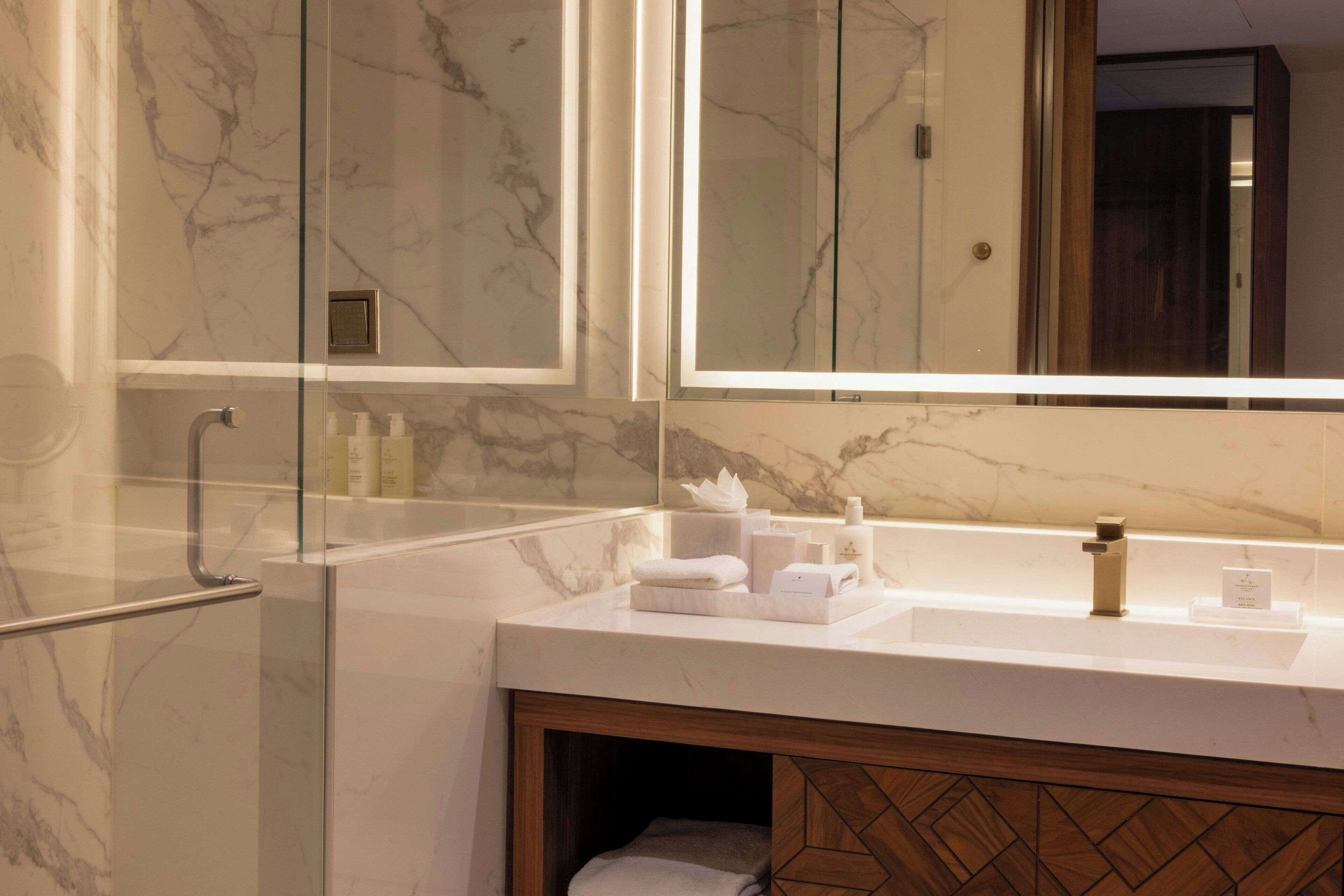 Un baño moderno con tocador de mármol, cabina de ducha de vidrio y mueble de madera.
